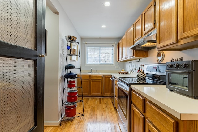 kitchen with under cabinet range hood, stainless steel appliances, a sink, light countertops, and brown cabinets