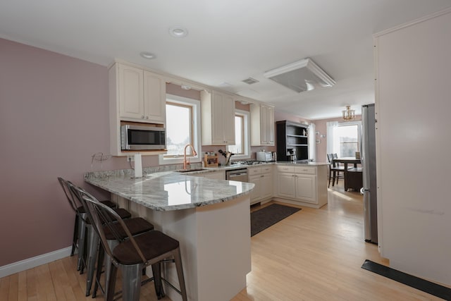 kitchen with light stone counters, a peninsula, a sink, white cabinetry, and appliances with stainless steel finishes