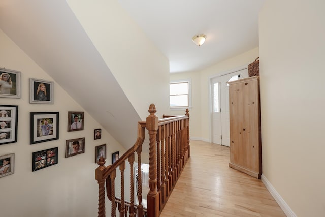 hallway featuring light wood-style floors, lofted ceiling, baseboards, and an upstairs landing