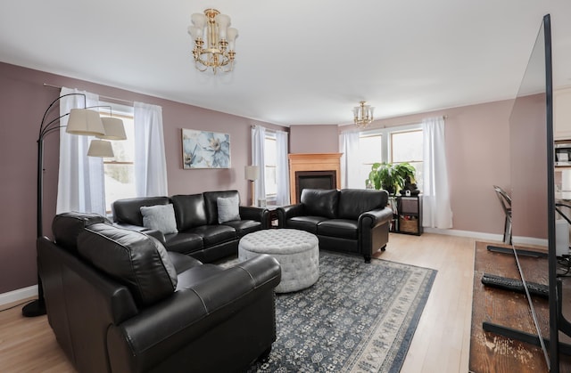 living area with light wood-type flooring, baseboards, a notable chandelier, and a glass covered fireplace