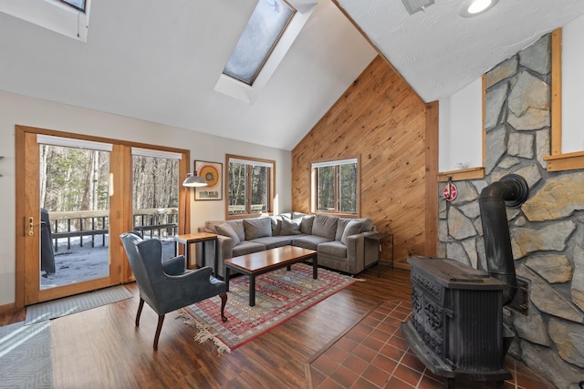 living room with a skylight, dark wood finished floors, a wood stove, wood walls, and high vaulted ceiling