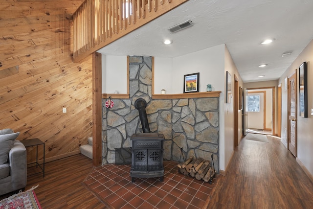 living area with a wood stove, wood walls, visible vents, and dark wood-type flooring