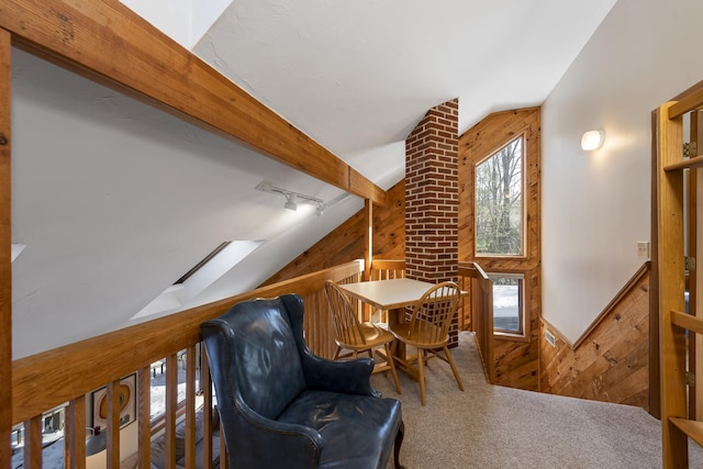 living area with vaulted ceiling with beams, rail lighting, carpet, an upstairs landing, and wood walls