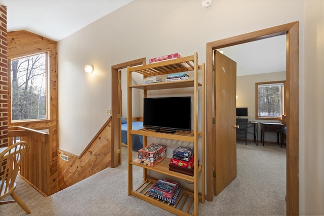 hallway with lofted ceiling, wood walls, light carpet, and an upstairs landing