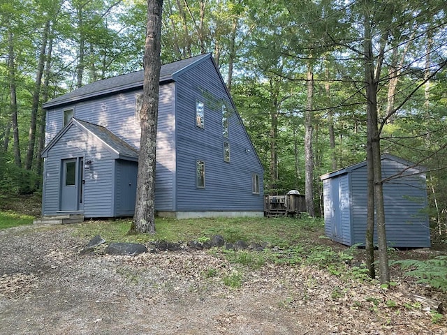 view of home's exterior with a shingled roof, entry steps, an outdoor structure, and a shed