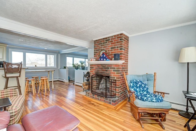 living area featuring crown molding, light wood finished floors, a baseboard heating unit, a brick fireplace, and a textured ceiling