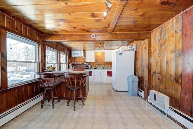 kitchen with light floors, a baseboard radiator, freestanding refrigerator, white cabinetry, and wood walls