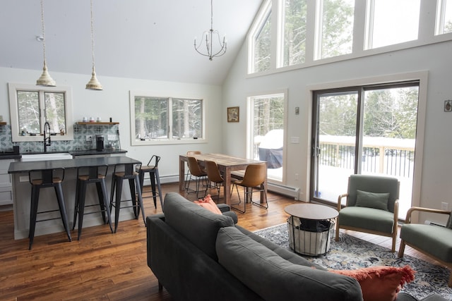 living room with high vaulted ceiling, a baseboard heating unit, an inviting chandelier, and wood finished floors