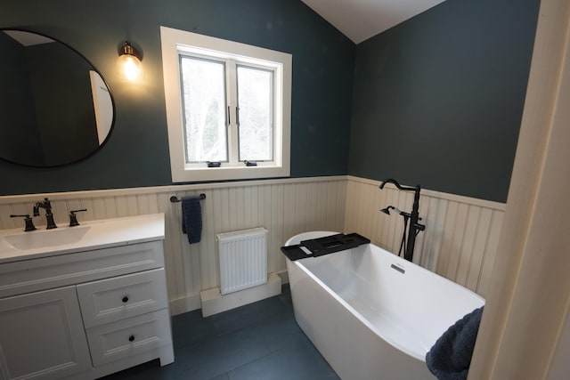 full bath with a wainscoted wall, radiator heating unit, a soaking tub, vaulted ceiling, and vanity