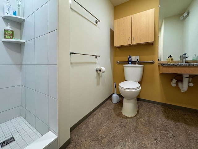 bathroom with toilet, a sink, baseboards, and tiled shower