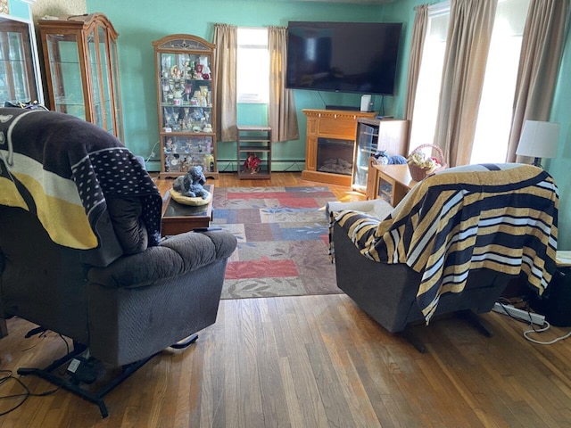 living room with a fireplace, a baseboard heating unit, and wood finished floors