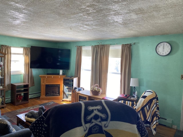 living room with a baseboard radiator, wood finished floors, a textured ceiling, a fireplace, and a baseboard heating unit