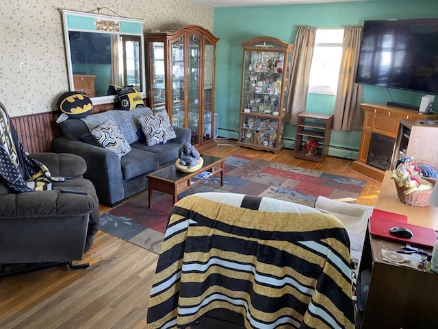 living area with a baseboard radiator, wood finished floors, a wainscoted wall, and wallpapered walls