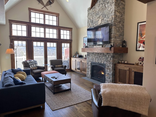 living room featuring dark wood-style floors, high vaulted ceiling, and a stone fireplace