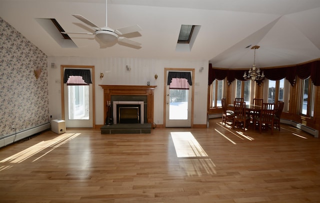 unfurnished living room featuring a fireplace with raised hearth, light wood-style flooring, a baseboard heating unit, ceiling fan with notable chandelier, and wallpapered walls