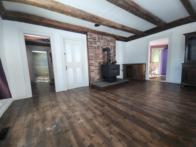 unfurnished living room featuring visible vents, baseboards, beam ceiling, dark wood finished floors, and a wood stove