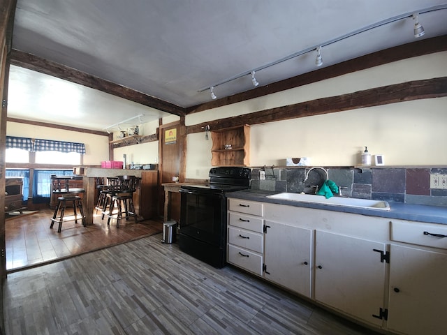 kitchen featuring black electric range oven, wood finished floors, beam ceiling, white cabinetry, and a sink