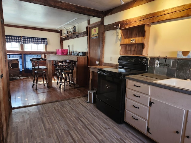 kitchen with black / electric stove, a sink, wood finished floors, white cabinetry, and beamed ceiling