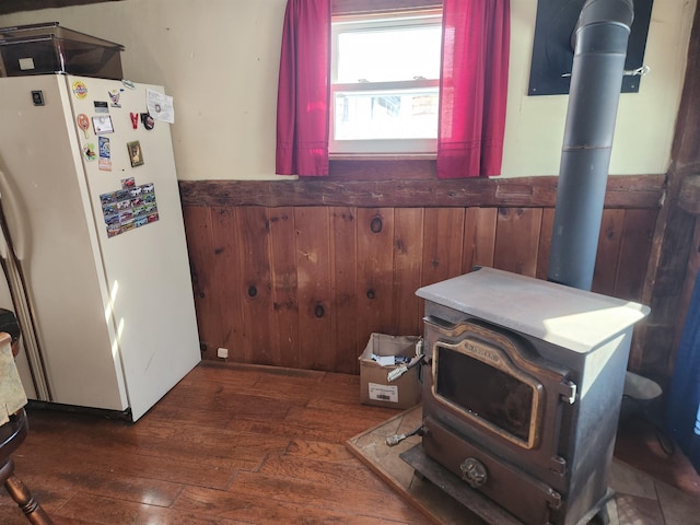 interior space with a wainscoted wall, wood walls, freestanding refrigerator, dark wood-style floors, and a wood stove