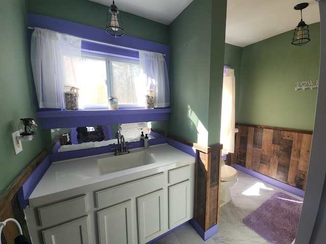 bathroom featuring toilet, wood walls, vanity, marble finish floor, and wainscoting