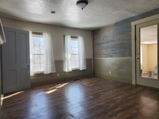 spare room with a wainscoted wall, dark wood-style flooring, visible vents, and wooden walls