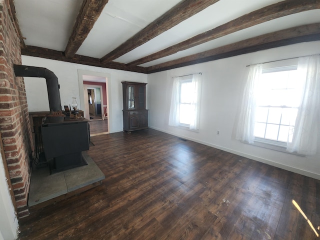 unfurnished living room featuring a wood stove, dark wood-style floors, baseboards, and beam ceiling