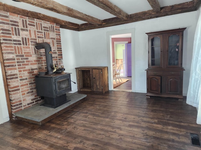 unfurnished living room featuring a wood stove, dark wood finished floors, and beam ceiling