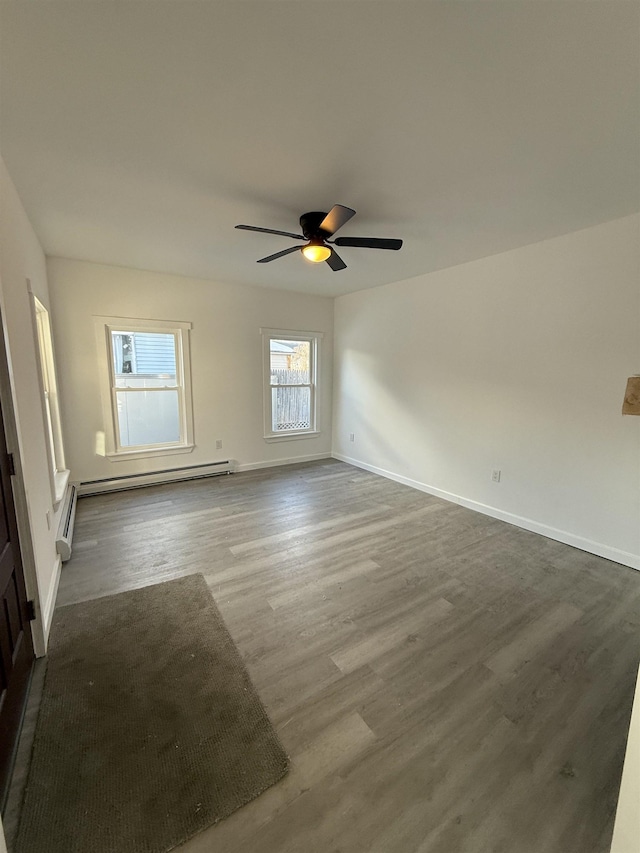 empty room with dark wood-type flooring, a baseboard heating unit, baseboards, and a ceiling fan