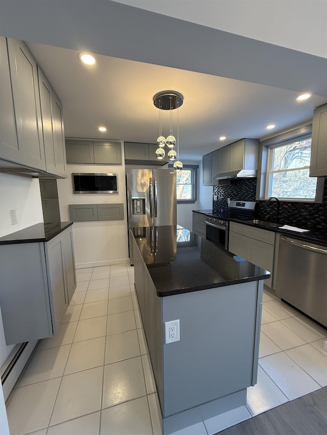 kitchen with dark countertops, appliances with stainless steel finishes, a center island, hanging light fixtures, and gray cabinetry