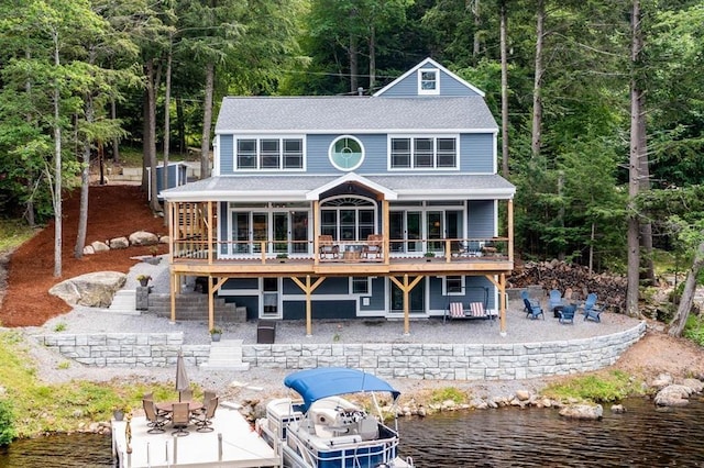 back of house featuring roof with shingles, a patio, a deck with water view, a fire pit, and stairs