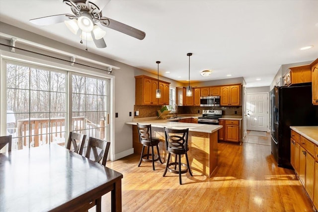 kitchen featuring appliances with stainless steel finishes, brown cabinets, a breakfast bar area, decorative light fixtures, and light countertops