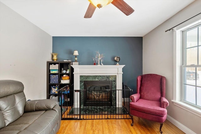 living room featuring ceiling fan, a premium fireplace, wood finished floors, and baseboards