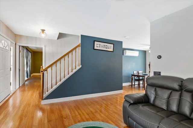 living room with ceiling fan, a wall unit AC, wood finished floors, baseboards, and stairway