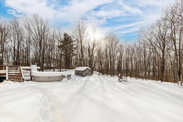 yard covered in snow featuring a storage shed, a deck, and an outbuilding