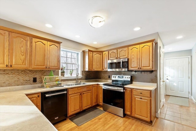 kitchen with stainless steel appliances, brown cabinetry, a sink, and light countertops