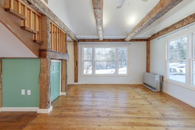 unfurnished living room with baseboards, ceiling fan, heating unit, light wood-style floors, and beam ceiling