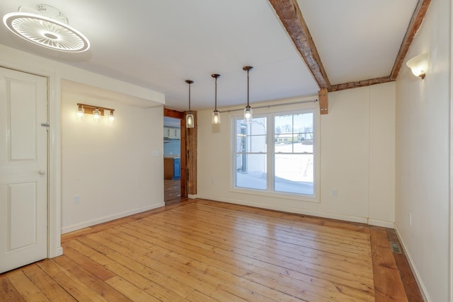 unfurnished dining area with light wood finished floors, beam ceiling, and baseboards