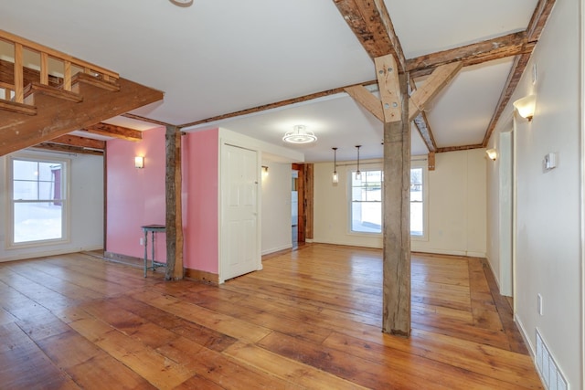 spare room featuring light wood-style floors, visible vents, beamed ceiling, and baseboards