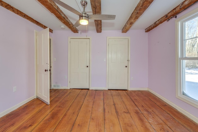 unfurnished bedroom with light wood-style flooring, visible vents, a ceiling fan, baseboards, and beam ceiling