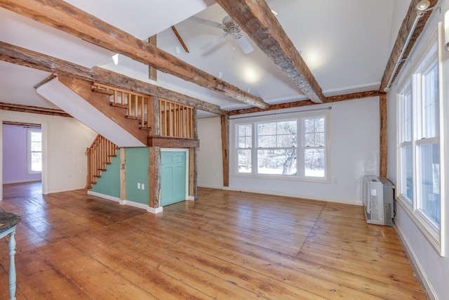 unfurnished living room featuring ceiling fan, baseboards, stairway, light wood-type flooring, and beamed ceiling