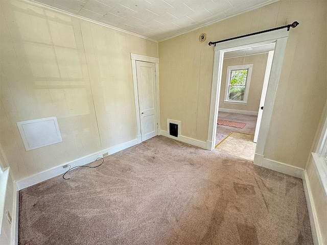 unfurnished room with light carpet, wood walls, visible vents, and baseboards