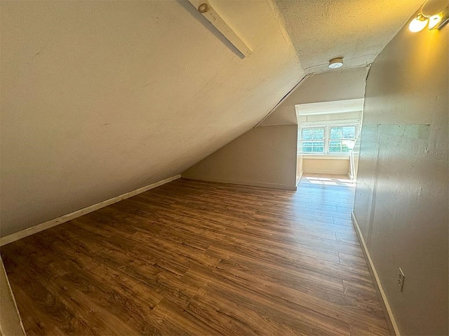 bonus room featuring lofted ceiling, a textured ceiling, wood finished floors, and baseboards