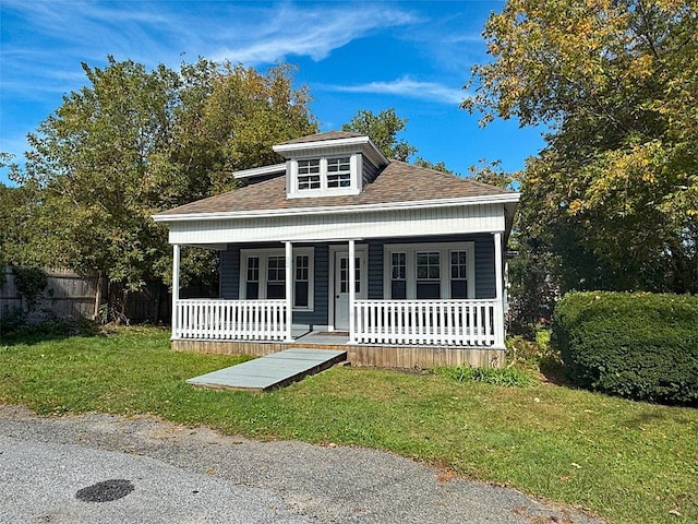 bungalow-style house featuring covered porch, a shingled roof, fence, and a front lawn