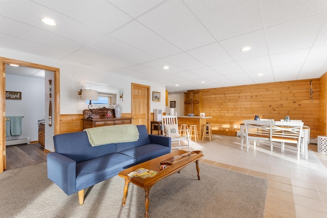 living room featuring light tile patterned floors, baseboard heating, and wooden walls