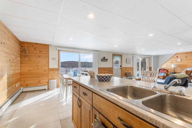 kitchen with light tile patterned floors, light countertops, open floor plan, a sink, and wooden walls