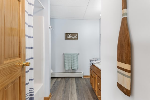 bathroom featuring a baseboard radiator, a paneled ceiling, toilet, vanity, and wood finished floors