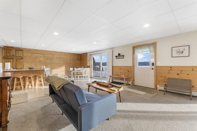 living area with a baseboard heating unit, a wainscoted wall, light carpet, and wooden walls