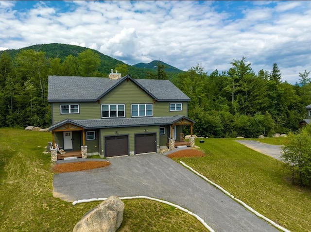 view of front of property featuring driveway, a chimney, an attached garage, a mountain view, and a front lawn