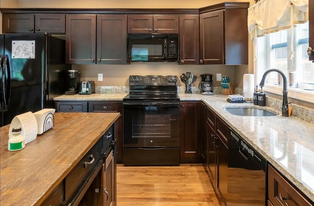 kitchen featuring light wood-style flooring, butcher block countertops, a sink, dark brown cabinets, and black appliances