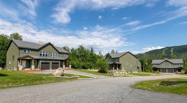 view of front of property with aphalt driveway, a chimney, an attached garage, a front yard, and a mountain view